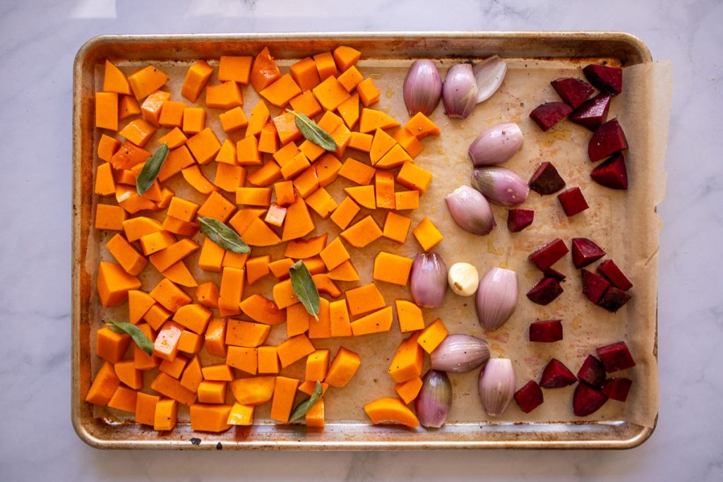 A baking sheet with butternut squash topped with sage, shallots, garlic and beets before roasting.