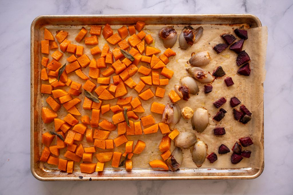 A baking sheet with roasted butternut squash topped with sage leaves, shallots, garlic, and beets.