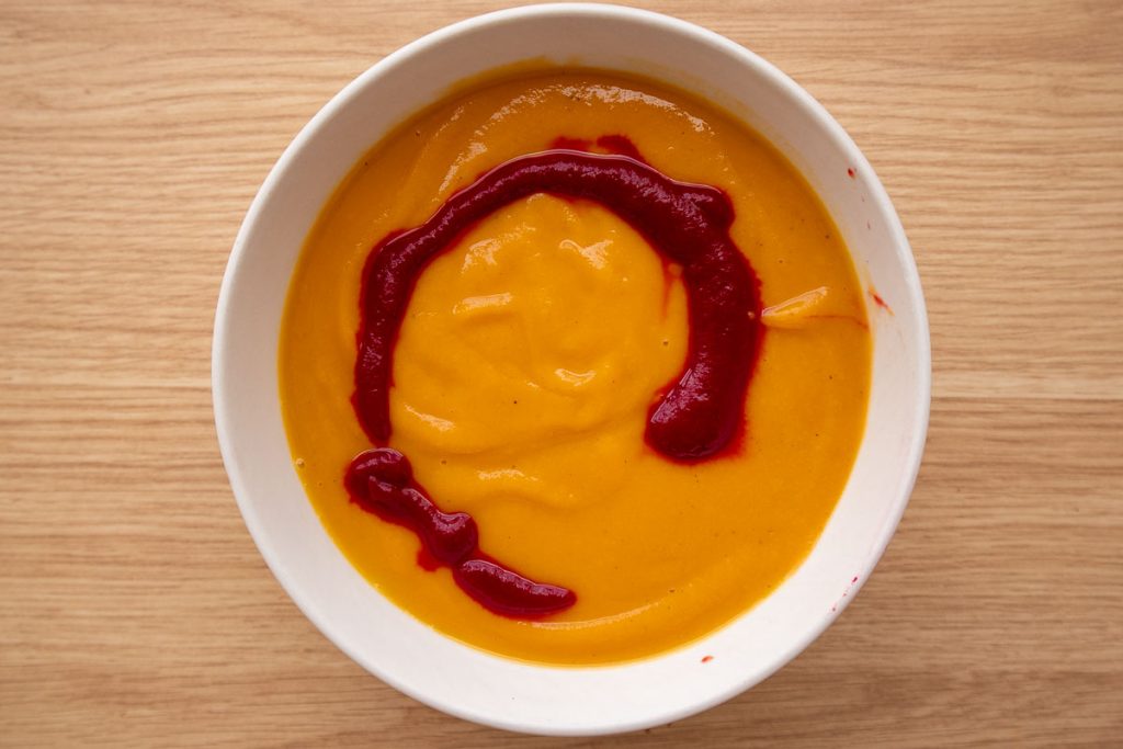 A white bowl with beet and butternut squash soup before the swirl.