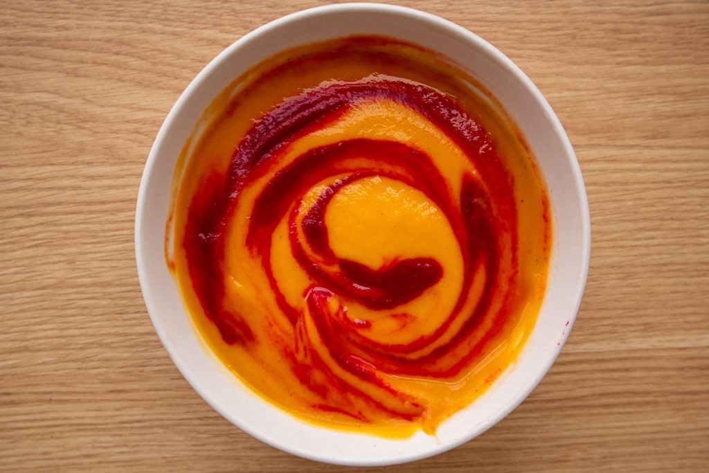 A white bowl with beet and butternut squash soup after the swirl.