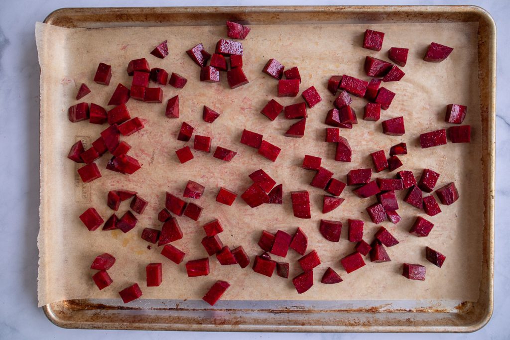A baking sheet topped with parchment paper and some uncooked chopped beets.