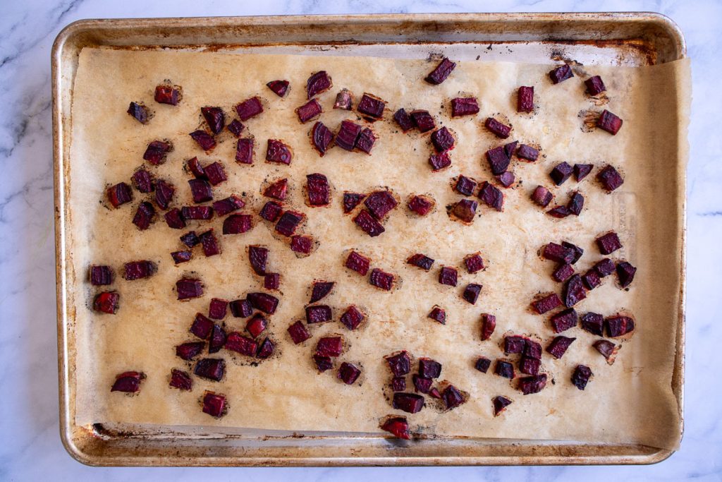 A baking sheet topped with parchment paper and some roasted beets.