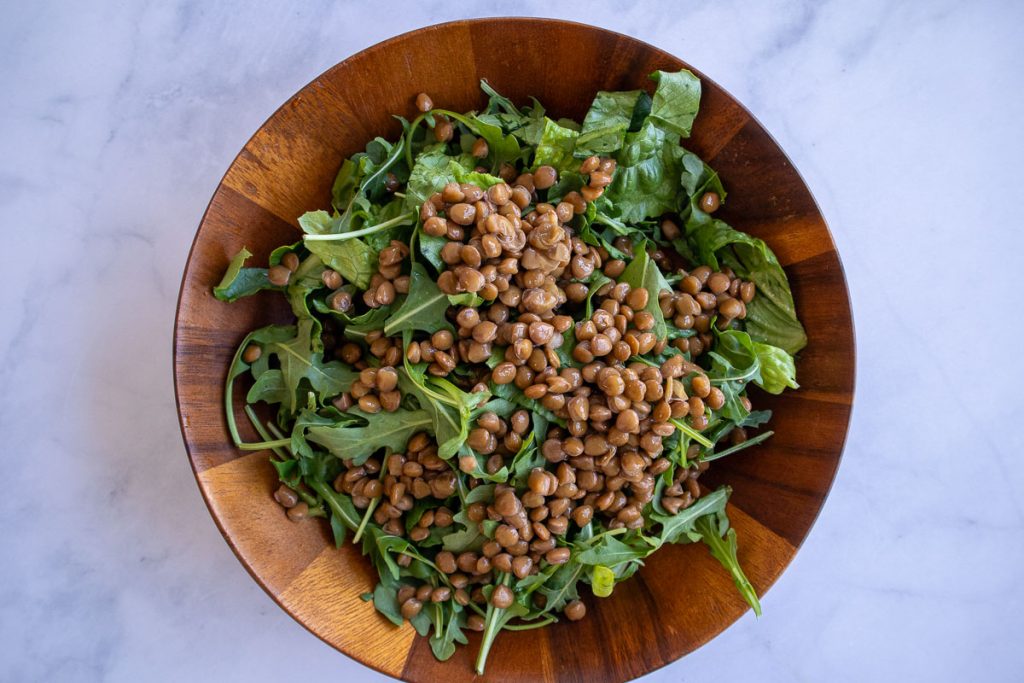 A wooden bowl with romaine, arugula and lentils.