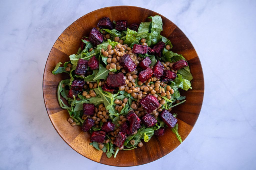 A wooden bowl with romaine, arugula, lentils and roasted beets.