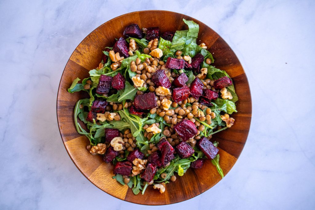 A wooden bowl with romaine, arugula, lentils, roasted beets and walnuts.