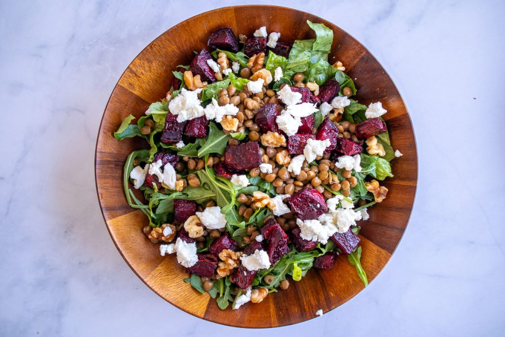 A wooden bowl with romaine, arugula, lentils, beets, walnuts and goat cheese.