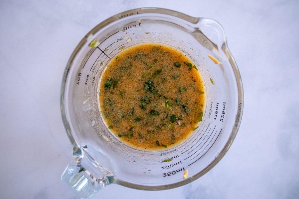 A measuring cup with tarragon vinaigrette mixed together.