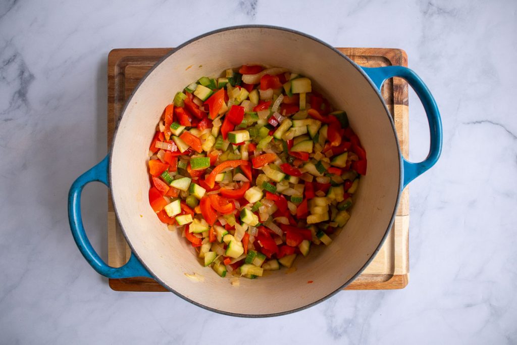 A blue soup pot with cooked onion, celery, bell pepper and zucchini.