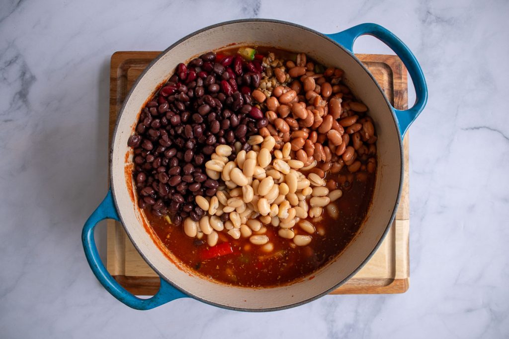 A blue soup pot with ingredients for five-bean chili after the beans have been added but not yet mixed in.