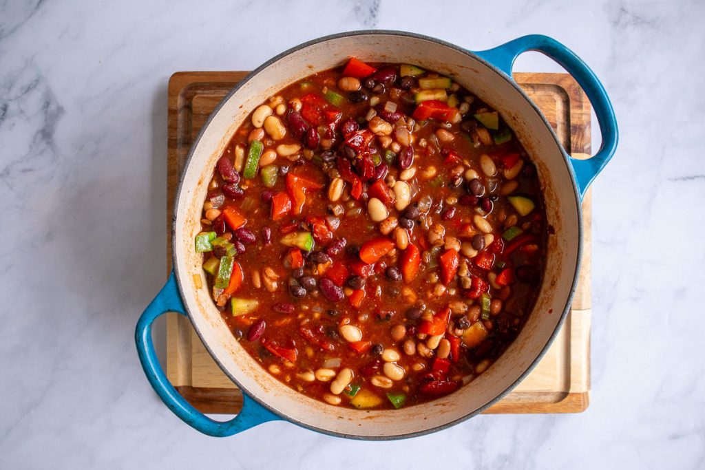 A blue soup pot with ingredients for five-bean chili after the beans have been added and mixed in but before simmering.