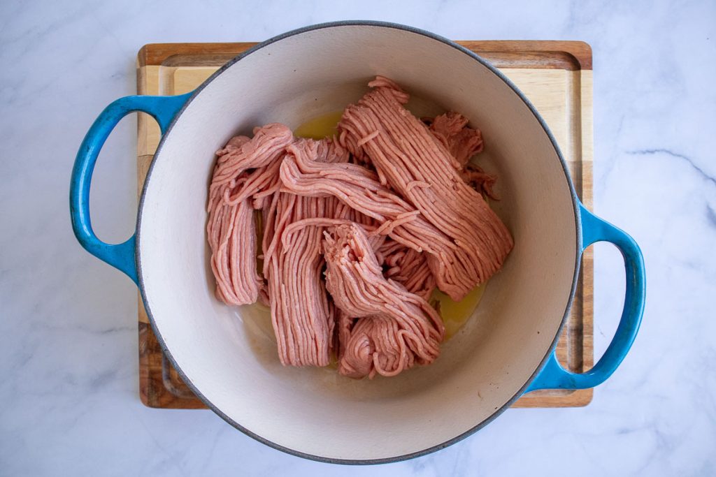 A blue soup pot with uncooked ground turkey in it.