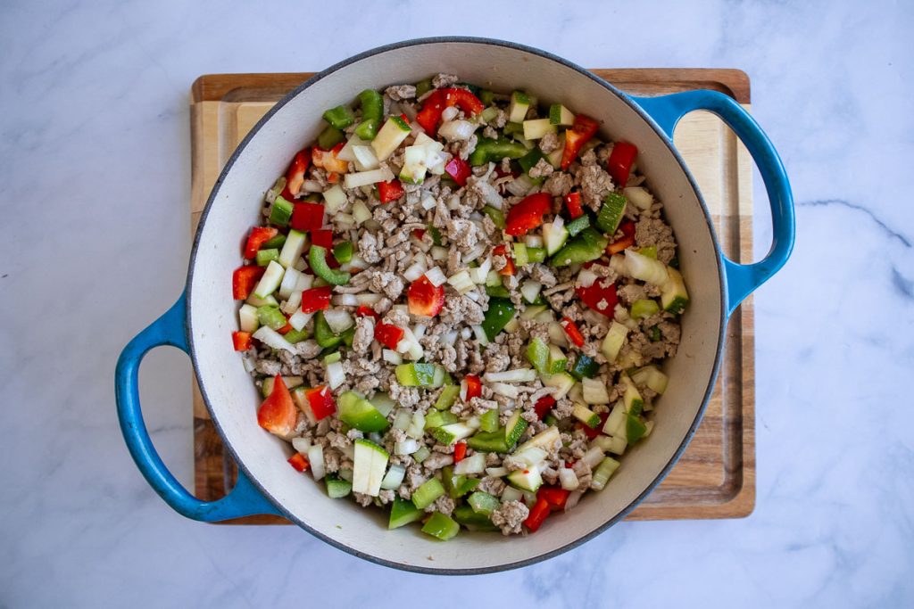 A blue soup pot with cooked ground turkey mixed with softened vegetables.