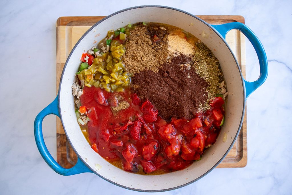 A blue pot with cooked ground turkey, vegetables, canned tomatoes, spices and chicken broth added but unmixed.