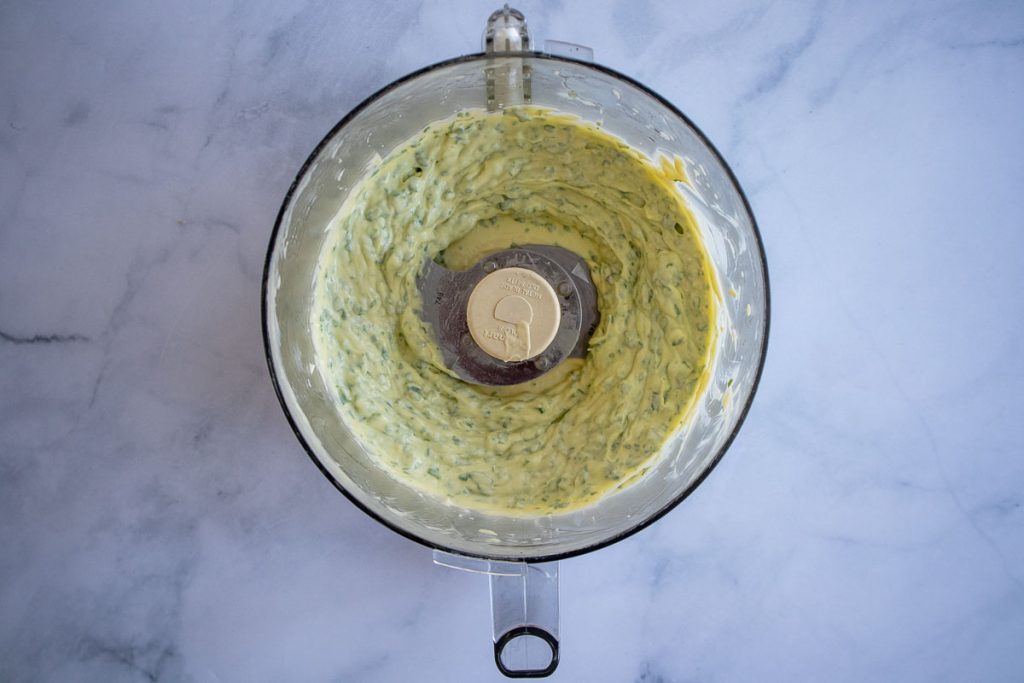 An overhead shot of a food processor bowl with finished basil mayonnaise inside.